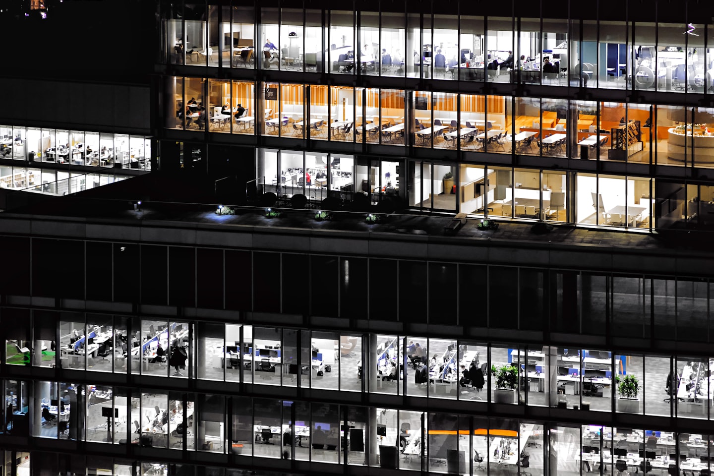 Modern office building lit up at night with employees working inside.